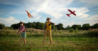 Twee kinderen staan in een veld en gooien zweefvliegtuigjes.