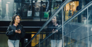 Een vrouw loopt een roltrap op met een telefoon in haar hand